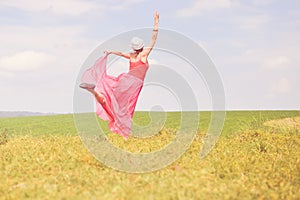 Joyful time outdoors: image of having fun elegant blond young woman in red dress happy dancing on green summer meadow copy space