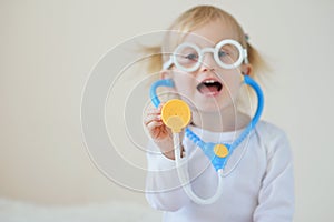 Joyful toddler girl playing as a doctor and hospital using stethoscope toy having fun at home.