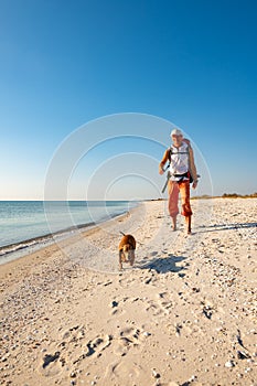 Joyful traveler with funny dog goes along the deserted beach