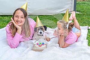 Joyful two girls sisters celebrating their dog's birthday with tasty cake in the garden