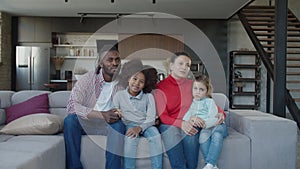 Joyful united multinational parents with cute mixed race daughters watching tv at home
