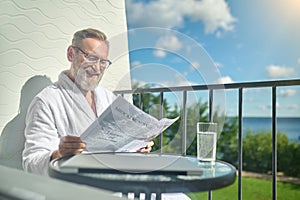 Joyful vacationer in eyeglasses reading good tidings in the newspaper