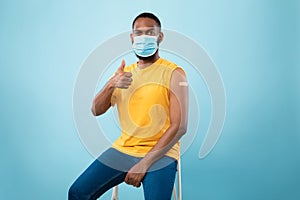 Joyful vaccinated black guy with adhesive plaster bandage on arm after coronavirus vaccine injection showing thumb up