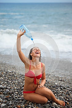 Joyful woman with bottle is sitting on coast
