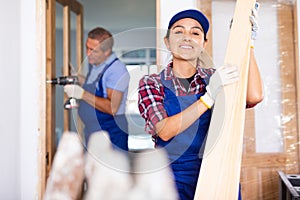 Joyful woman builder carrying wooden planks in apartment