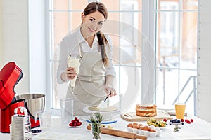 Joyful woman covering cream on the cake