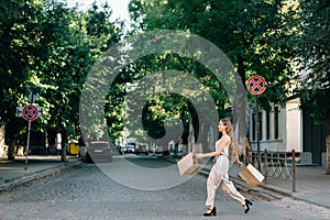 Joyful woman crosses the road with two shopping bags in both hands, beautiful gait