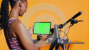 Joyful woman following tutorial videos on mockup tablet, learning to mend bike