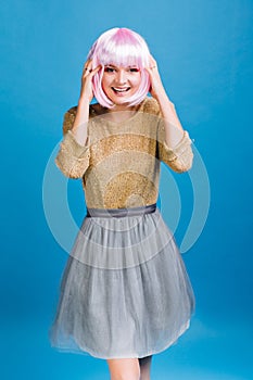 Joyful woman in golden brightful sweater, grey tulle skirt with pink cut hair having fun on blue background. Makeup with