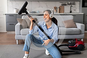 Joyful woman with headphones singing into vacuum cleaner