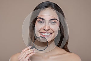 Joyful woman holding magnifier near jawline