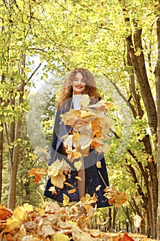 Joyful woman kicks autumn leaves with her foot