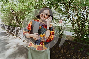 Joyful woman with laptop talking on phone in park