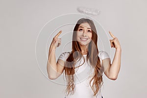 Joyful woman pointing at holy nimbus over head, showing aureole and looking up with toothy smile.