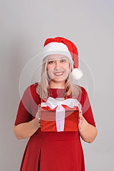 A joyful woman in a Santa hat holds a red gift box in her hands, vertical photo
