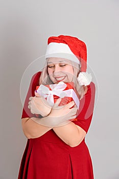 A joyful woman in a Santa hat hugs a red gift box, vertical photo