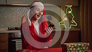 Joyful Woman in Santa Hat Receives Exciting News via Smartphone During Christmas Celebration