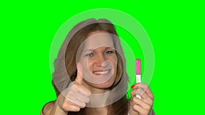Joyful woman showing positive pregnancy test and thumbs up gesture at camera