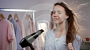 Joyful woman singing in hair dryer. Emotional woman singing in bathroom