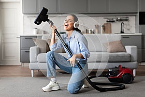 Joyful woman singing with vacuum cleaner during house chores