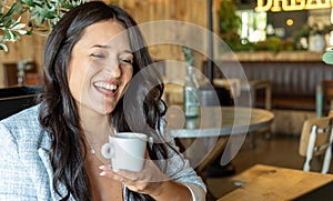 Joyful woman smiling while enjoying drinking a cup of coffee in a coffee shop