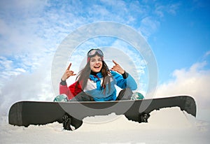 Joyful woman snowboarder sitting on top of mountain on blue sky