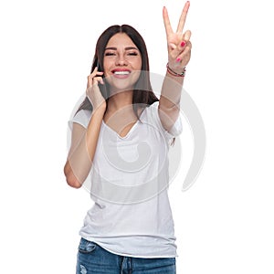 Joyful woman speaking on the phone and making victory sign