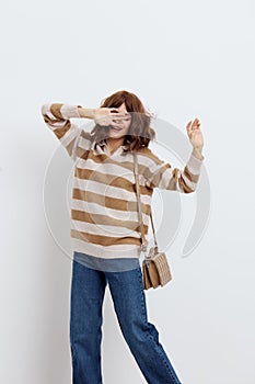 a joyful woman stands on a white background in a striped sweater and with a bag on her shoulder, she closed one eye with