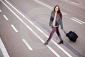 Joyful woman with suitcase crossing the street