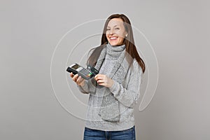 Joyful woman in sweater, scarf hold wireless modern bank payment terminal to process, acquire credit card payments