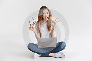 Joyful woman in t-shirt sitting on floor with laptop computer