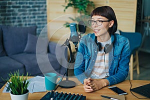 Joyful woman talking in microphone working at table in recording studio