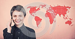 Joyful woman talking on phone abroad, smiling over pink wall with world map. Trendy positive tourist girl speak on smartphone in