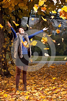 Joyful woman throwing autumn leaves