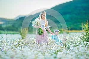 Joyful woman walk on green yellow flowering field background, rest, have fun, play, toss up little cute child baby boy. Mother,