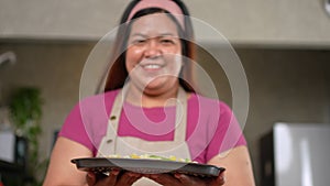 A joyful woman wearing apron standing in kitchen and holding pizza before baking. Making dough by hand in a bakery. Preparing