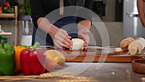 A joyful woman wearing apron standing in kitchen and kneading pizza dough on table. Making dough by hand in a bakery. Preparing