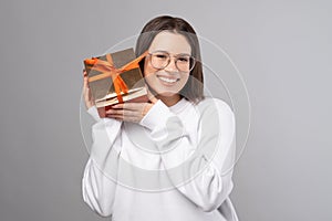 Joyful woman wearing glasses is holding a red gift box near her face.