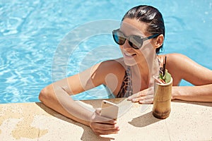 Joyful woman wearing swimming pool and black sunglasses, having fun and bathing in hotel resort spa pool, drinking fresh cocktail