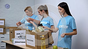 Joyful women in volunteer t-shirts putting food in boxes, provision donation