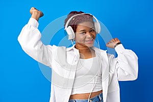 Joyful young african american woman listening to music with headphones against blue background