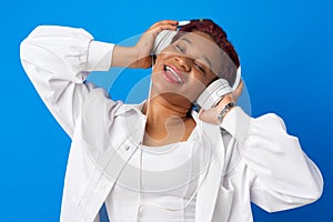 Joyful young african american woman listening to music with headphones against blue background