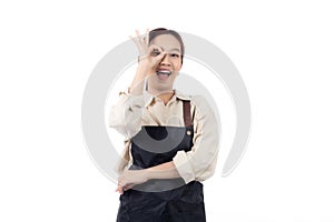 Joyful young asian woman wearing apron is barista attire gesturing OK with her hand, expressing satisfied and approval.