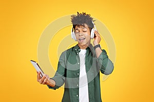 Joyful young black guy listening to music on yellow background