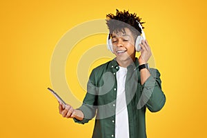 Joyful young black guy listening to music, using app
