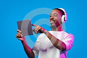 Joyful young black guy using wireless headset and digital pad