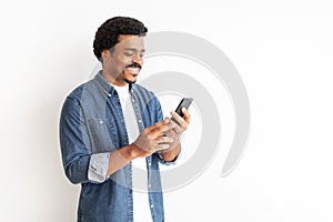 Joyful young black man in denim engaging with smartphone