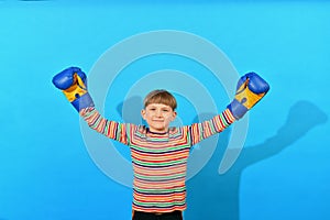 A joyful young boxer in blue gloves raised his hands up in a sign of victory over an opponent