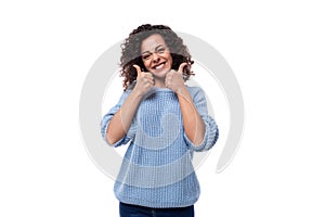 joyful young brunette woman with curls dressed in a blue knitted sweater smiling on a white background