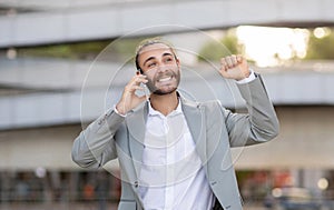 Joyful young businessman celebrating success during outdoor phone call